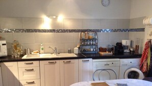 A compact kitchen with a sink, dishwasher, and a small table with a cutting board and utensils.