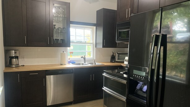 A modern kitchen with dark cabinets, stainless steel appliances, a dishwasher, and a window providing natural light. - 3-bedroom vacation home just 20 minutes from Six Flags St. Louis (Ballwin)