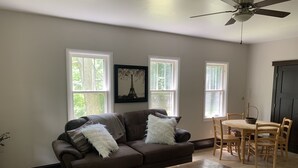 A living room with a brown sofa, a wooden coffee table, and a dining table with chairs. There are three windows providing natural light. - 3-bedroom vacation home just 20 minutes from Six Flags St. Louis (Ballwin)