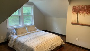 A bedroom with a sloped ceiling, a bed with striped bedding, a window, and a painting of a tree. - 3-bedroom vacation home just 20 minutes from Six Flags St. Louis (Ballwin)