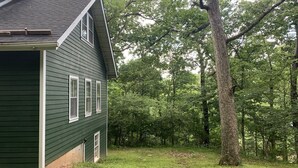 A green house with a sloped roof and a garage door, surrounded by a grassy yard and trees. - 3-bedroom vacation home just 20 minutes from Six Flags St. Louis (Ballwin)
