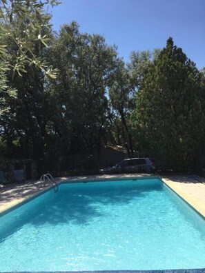 A rectangular swimming pool with clear blue water, surrounded by trees and a stone wall. - Gîte Hameau de Pomples (CABASSE)