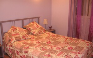 A bedroom with a bed, a nightstand, a lamp, and a window with curtains. - Gîte Hameau de Pomples (CABASSE)