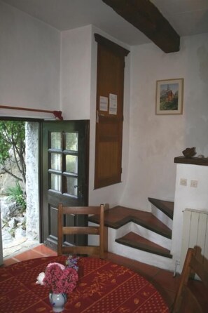 Une pièce avec un escalier en bois, une table ronde agrémentée d’un arrangement floral et une fenêtre donnant sur un paysage verdoyant.