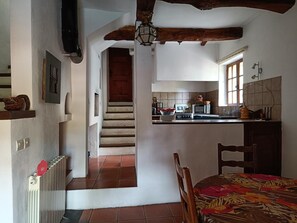 A kitchen with a dining area, a staircase leading to another room, and a radiator on the wall. - Le Gîte Panda Saint-maymes (TRIGANCE)