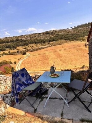 An outdoor seating area with a table, chairs, and a view of a hilly landscape. - Le Gîte Panda Saint-maymes (TRIGANCE)