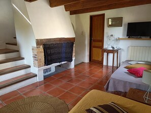Een kamer met een open haard, een bed met kussens, een televisie en een tafel met een ventilator.