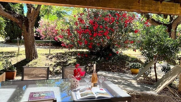 An outdoor table set up under a wooden pergola with a book, a bottle, and glasses on it. - Les Roses Rouges - SIX Fours LES Plages (SIX FOURS LES PLAGES)