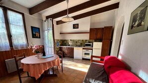 A cozy room with a round table, a red sofa, and a kitchen area with wooden cabinets and appliances. - Les Roses Rouges - SIX Fours LES Plages (SIX FOURS LES PLAGES)