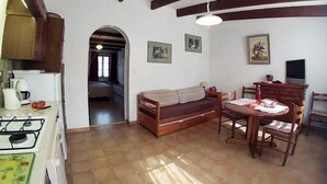 A cozy living area with a sofa, dining table, and kitchen area including a stove and coffee maker. - Les Roses Rouges - SIX Fours LES Plages (SIX FOURS LES PLAGES)