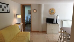 A living room with a yellow sofa, a small table, a TV on a cabinet, and a mirror on the wall.