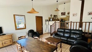 A spacious living area with a wooden dining table, black leather sofa, and a kitchen in the background.