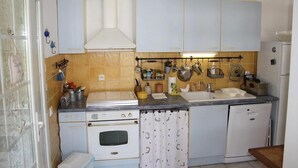 Una cocina compacta con estufa, horno y lavavajillas. Hay armarios sobre la encimera y un tendedero con ollas y sartenes.