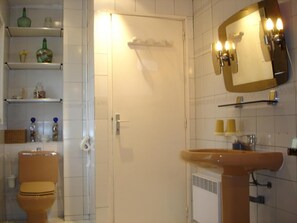 A bathroom with a toilet, sink, mirror, shelves with toiletries, and a towel rack.