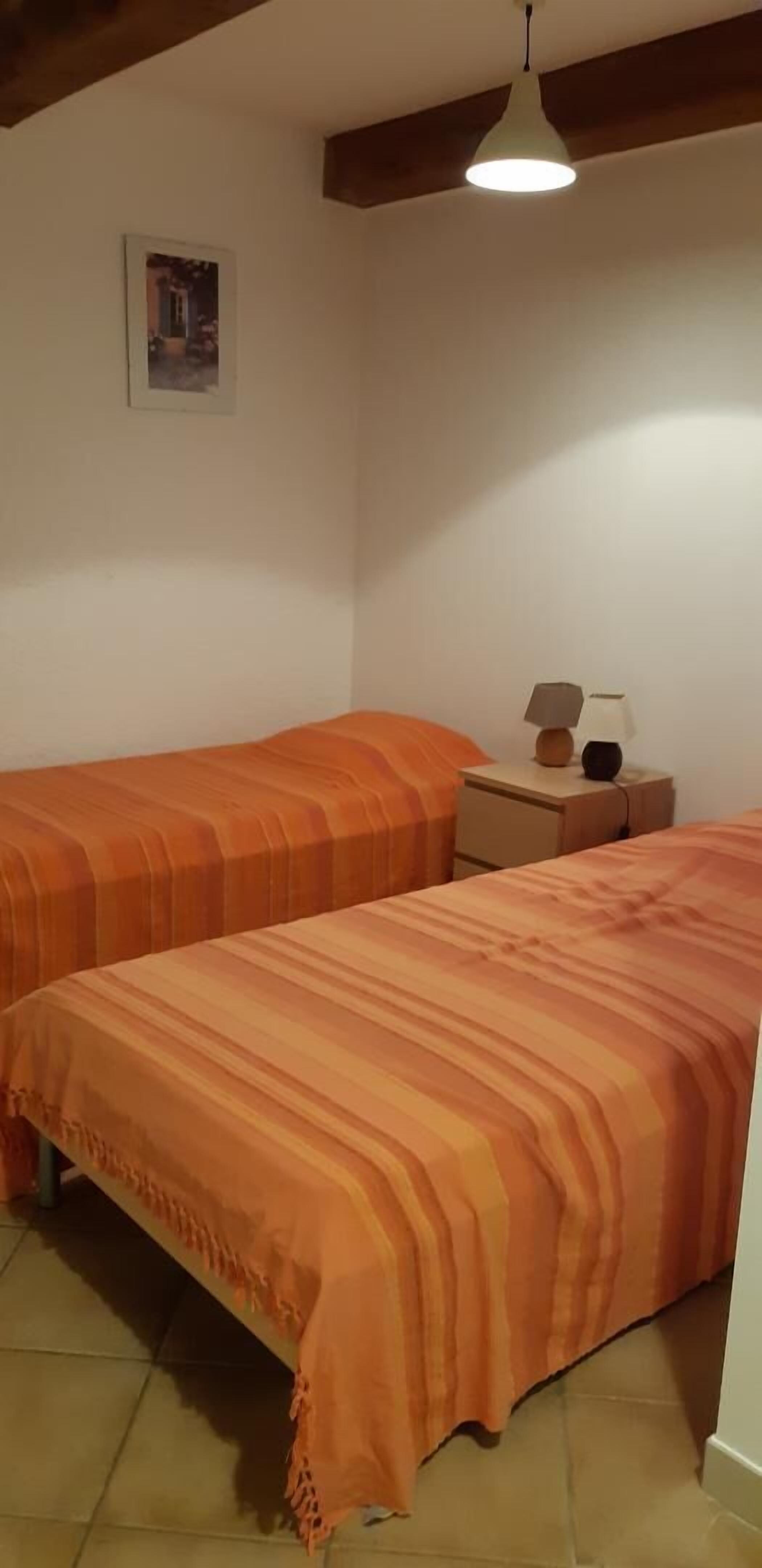 A bedroom with two beds, a nightstand, a lamp, and a picture on the wall.