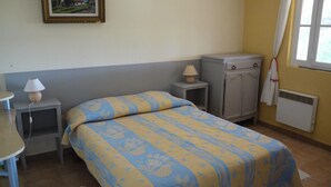 Quarto com cama, mesas de cabeceira, abajur, guarda-roupa e janela com cortinas.