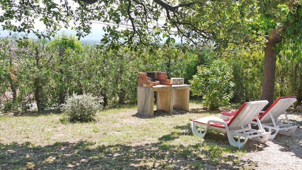 Um jardim com mesa e cadeiras, cercado por árvores e arbustos.