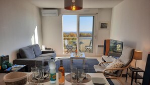 Un salón moderno con un sofá, una mesa de comedor para dos personas y un balcón con vistas a la ciudad.