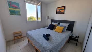 A bedroom with a bed, pillows, a nightstand, a lamp, a small wooden stool, and two paintings on the wall.