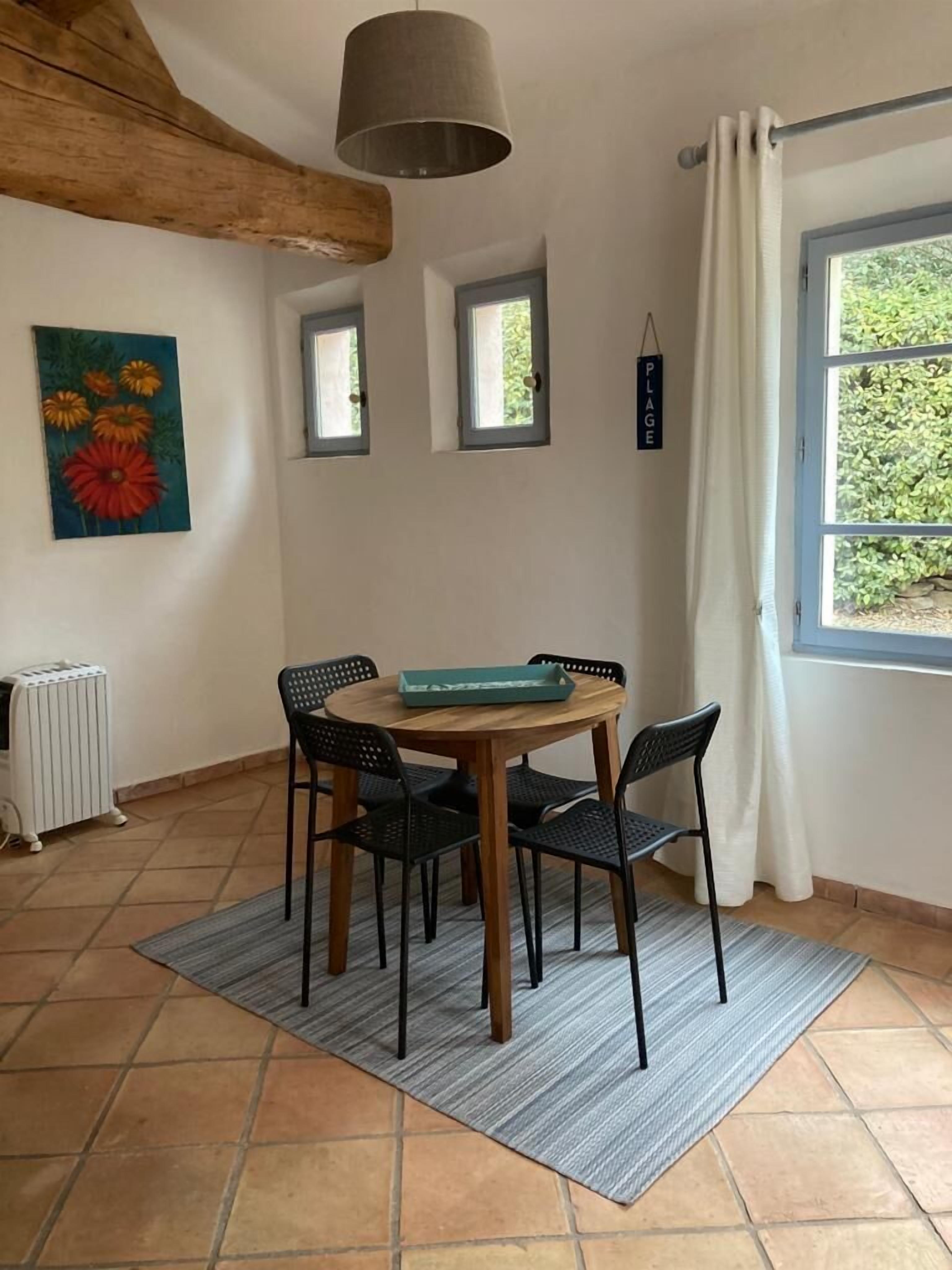 Un coin repas comprenant une table en bois, quatre chaises, un luminaire suspendu, un radiateur et une fenêtre avec des rideaux.