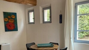 Ruokailutila, jossa on puinen pöytä, neljä tuolia, riippuvalaisin, patteri ja ikkuna, jossa on verhot.