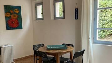 Un coin repas comprenant une table en bois, quatre chaises, un luminaire suspendu, un radiateur et une fenêtre avec des rideaux.