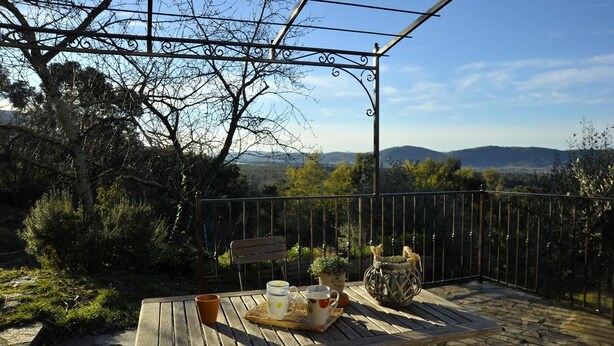 Une table en bois, accompagnée d’un banc et de plantes en pot, placée devant un paysage pittoresque composé d’arbres et de montagnes.
