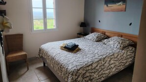 Une chambre à coucher comprenant un lit, une chaise, une table de chevet, une lampe et une fenêtre donnant sur un beau paysage.