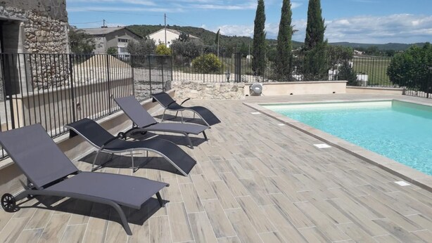 Zona junto a la piscina con sillones de descanso y una piscina, rodeada de muros de piedra y un edificio de piedra.