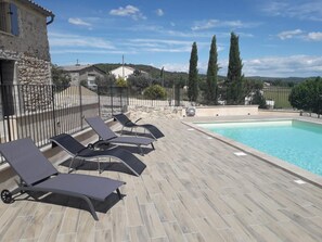 A poolside area with lounge chairs and a swimming pool, surrounded by stone walls and a stone building.