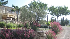 Un muro de piedra con flores rosadas, un camino de grava y un edificio con balcón.