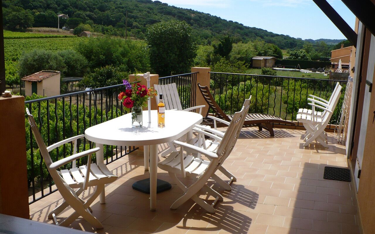 A balcony with a round table, white chairs, and a vase of flowers.