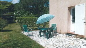 Une terrasse extérieure avec un sol en pierre, une table entourée de chaises et un parasol à rayures.