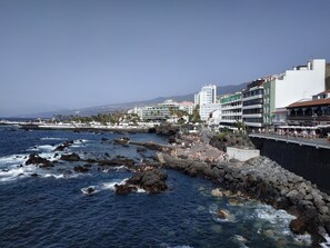 En kuststad med en bergig strandlinje, en strandpromenad full av människor och byggnader i bakgrunden.