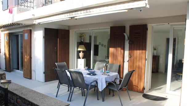 An outdoor dining area with a table and chairs, a lamp, and a view of the interior through glass doors. - Joli T3 Face MER - LES Issambres (LES ISSAMBRES)