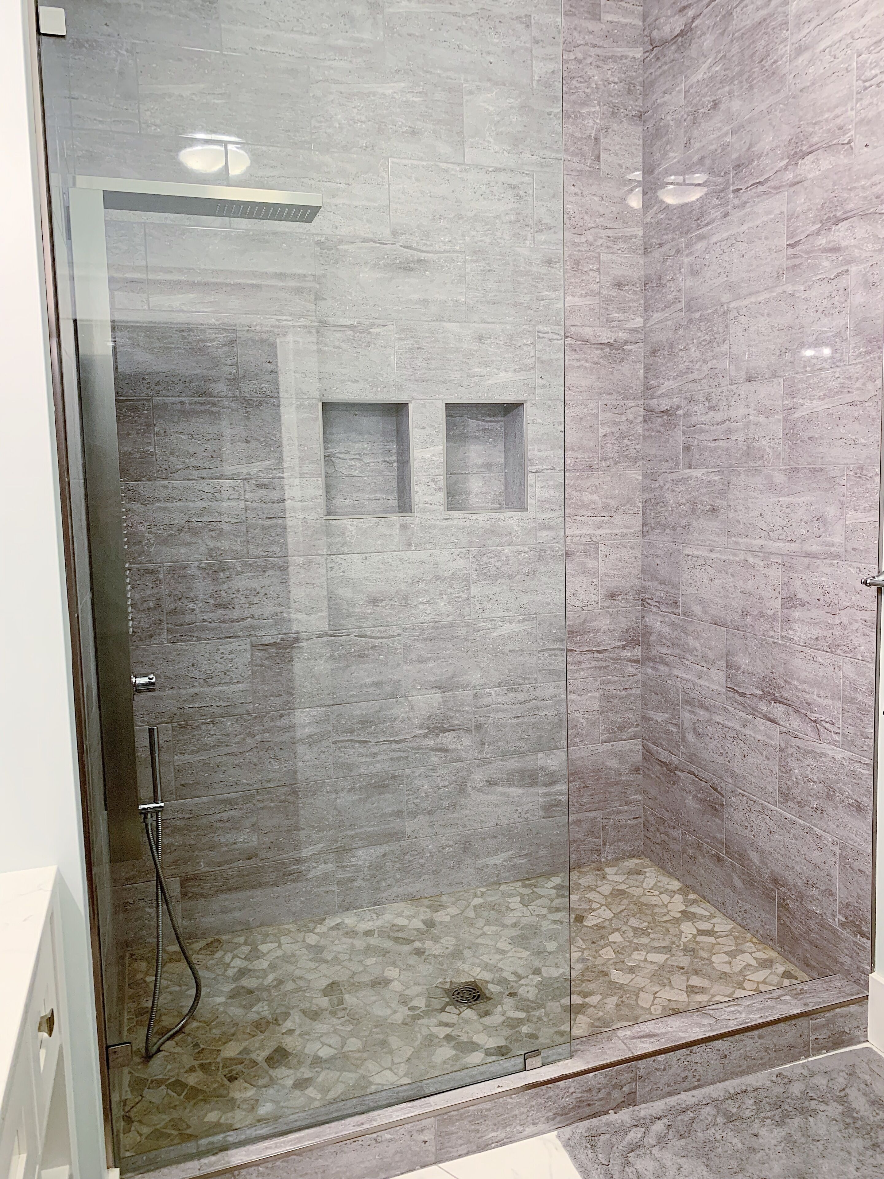 A glass-enclosed shower with a tiled floor and a showerhead.