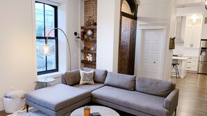 A modern living room with a sectional sofa, a round coffee table, and a brick accent wall. - Downtown Heritage Condo (Charlottetown)