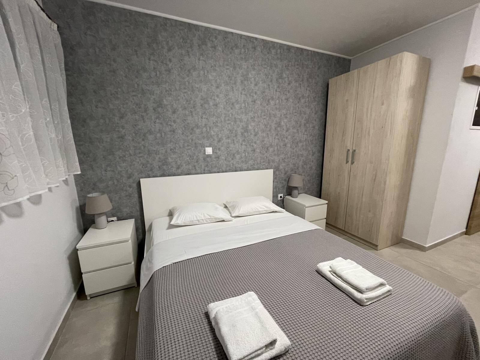 A bedroom with a bed, two nightstands, a wardrobe, and a grey textured wall.