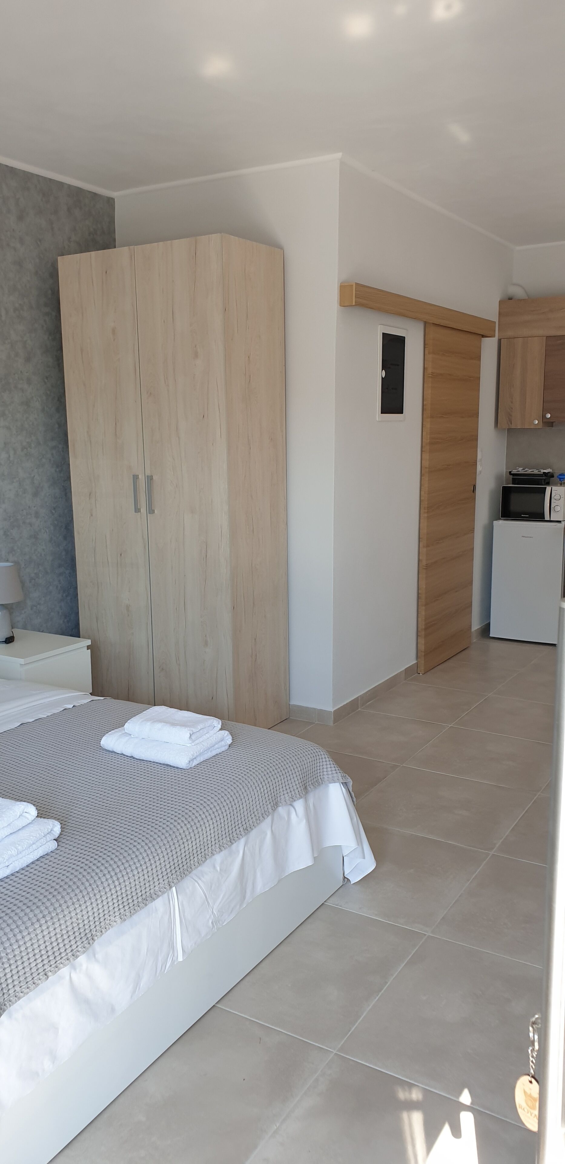 Une chambre moderne avec un grand lit, une armoire en bois et une petite kitchenette.
