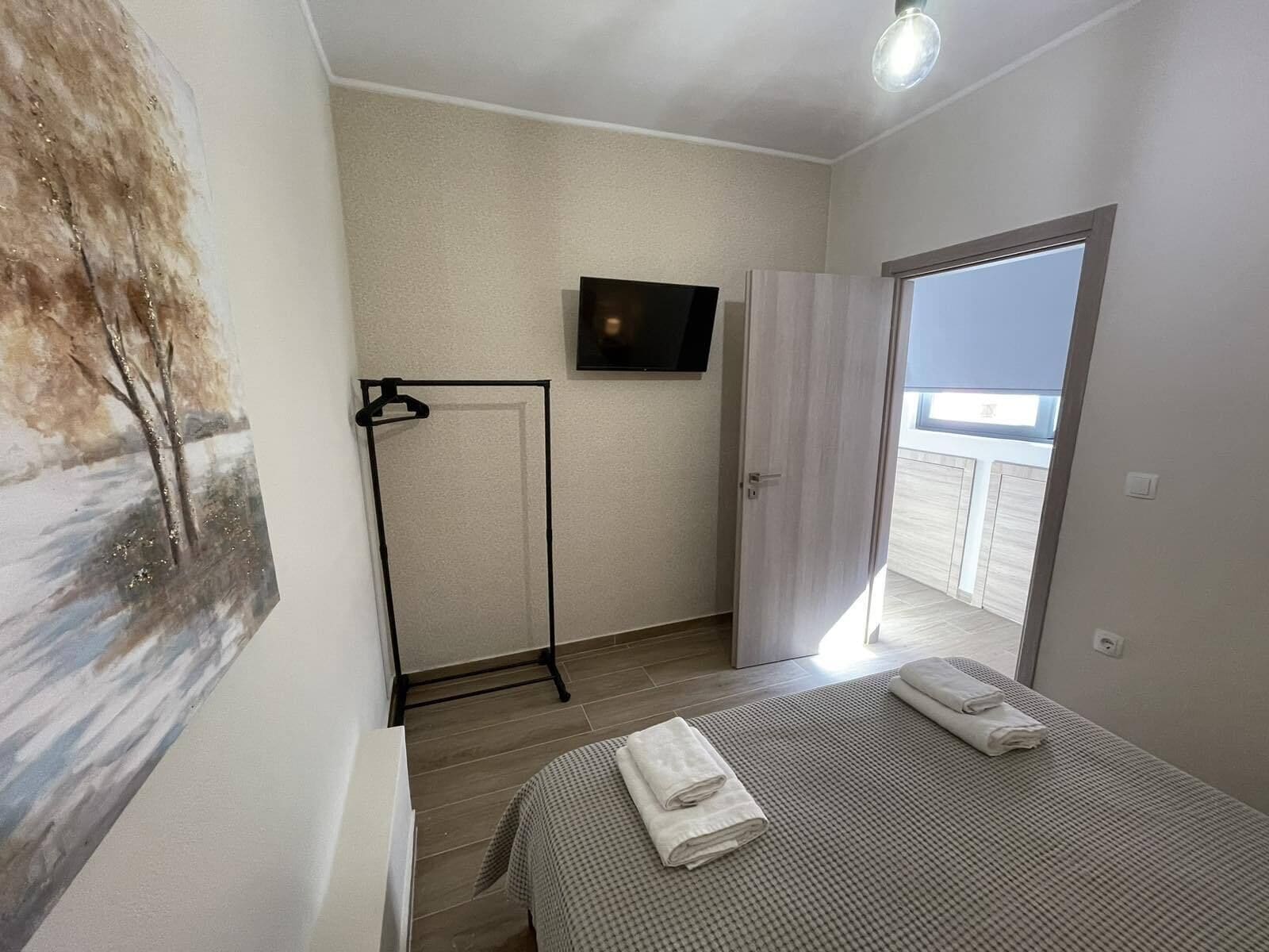 A hotel room with a bed, a painting on the wall, a TV, and a door leading to a balcony.