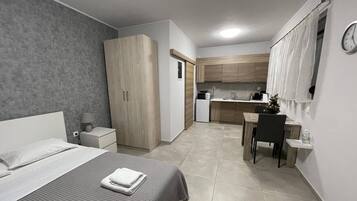 A modern hotel room with a bed, bedside table, and a small kitchenette.