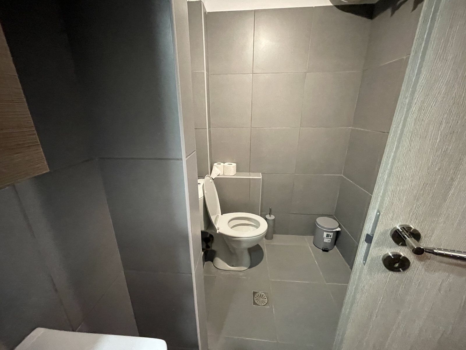 Un baño pequeño y moderno con inodoro, un cesto de basura y zona de ducha.