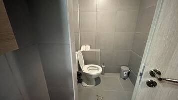 Un baño pequeño y moderno con inodoro, un cesto de basura y zona de ducha.