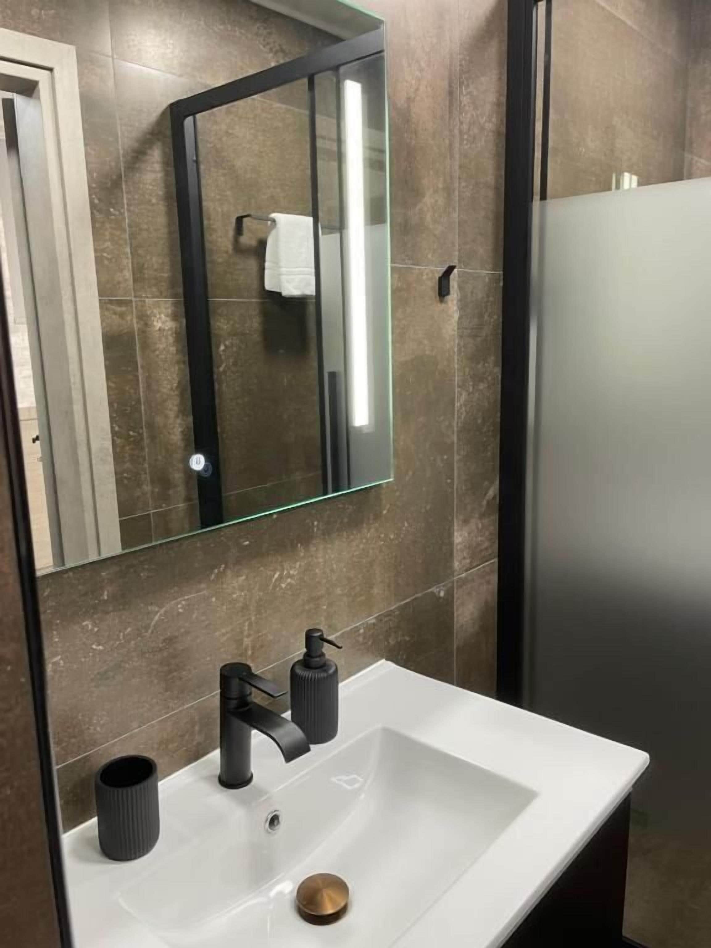 Un baño moderno con un lavamanos blanco, grifo negro y un espejo con marco negro.