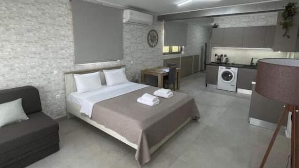 A modern bedroom with a bed, bedside table, and a small desk. There is a dark-colored sofa and a large mirror. The room has a neutral color scheme and a modern design. - AVR DELUXE SUITES 6 AIRPORT FREE SHUTTLE (Markopoulo Mesogaias)