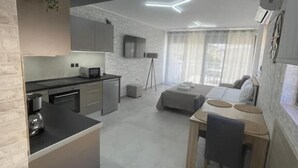 A modern kitchen with a central island, a dining area with a table and chairs, and a living space with a sofa and a TV. - AVR DELUXE SUITES 6 AIRPORT FREE SHUTTLE (Markopoulo Mesogaias)