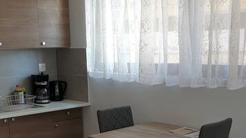 A modern kitchen with wooden cabinets, a dining table with chairs, and a window with sheer curtains.