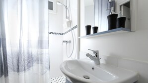 Une salle de bain avec un lavabo blanc, une douche et un miroir au-dessus du lavabo.