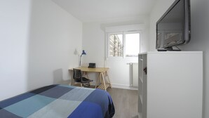 Une chambre à coucher avec un lit, un bureau, une chaise, une télévision et une fenêtre.
