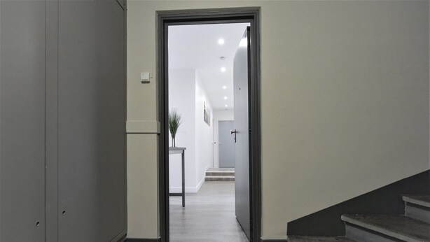 Un couloir avec un paillasson, un escalier et une porte donnant sur une autre pièce.